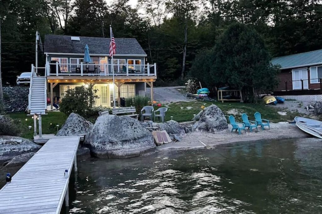 A lakeside cabin with a dock, outdoor seating, and a flag.