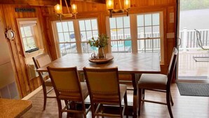 A wooden dining area with a table and chairs, large windows, and a view of the outside.
