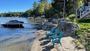 A lakeside property with a dock, clear water, and a sandy beach with chairs.