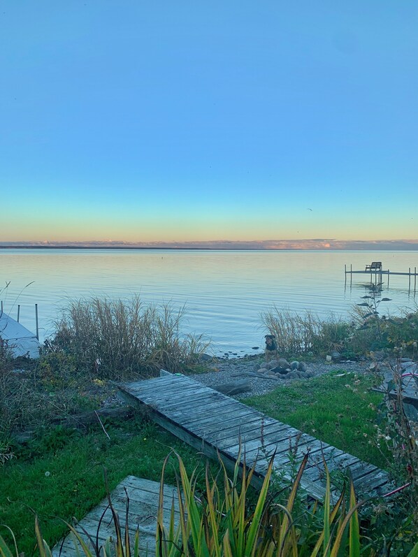 A calm lake with a wooden dock extending into the water, surrounded by grassy areas and some vegetation. - Cozy Lake House on Oneida with Waterfront Access (Cicero)