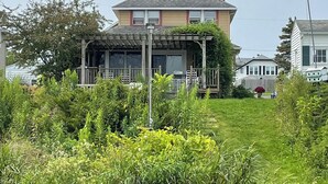 A residential house with a porch, a grassy yard, and a dock extending into a body of water. - Cozy Lake House on Oneida with Waterfront Access (Cicero)