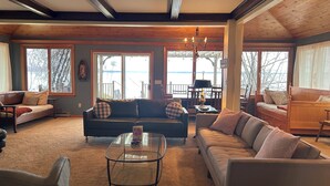 A cozy living room with a sofa, armchairs, and a glass coffee table. Large windows offer a view of the outdoors. - Cozy Lake House on Oneida with Waterfront Access (Cicero)