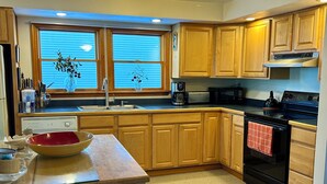 A kitchen with wooden cabinets, a sink, a stove, and a window with blinds. - Cozy Lake House on Oneida with Waterfront Access (Cicero)
