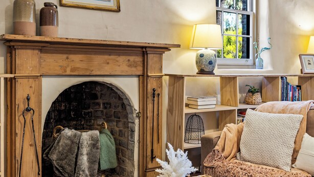 A cozy living room with a fireplace, a comfortable sofa, a bookshelf, and a window with a view of greenery. - Idyllic, peaceful and historical "Coath Cottage" minutes from Bendigo's CBD (West Bendigo)