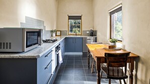 A compact kitchen with a microwave, stove, and sink, a dining table with chairs, and a window with a view of greenery. - Idyllic, peaceful and historical "Coath Cottage" minutes from Bendigo's CBD (West Bendigo)