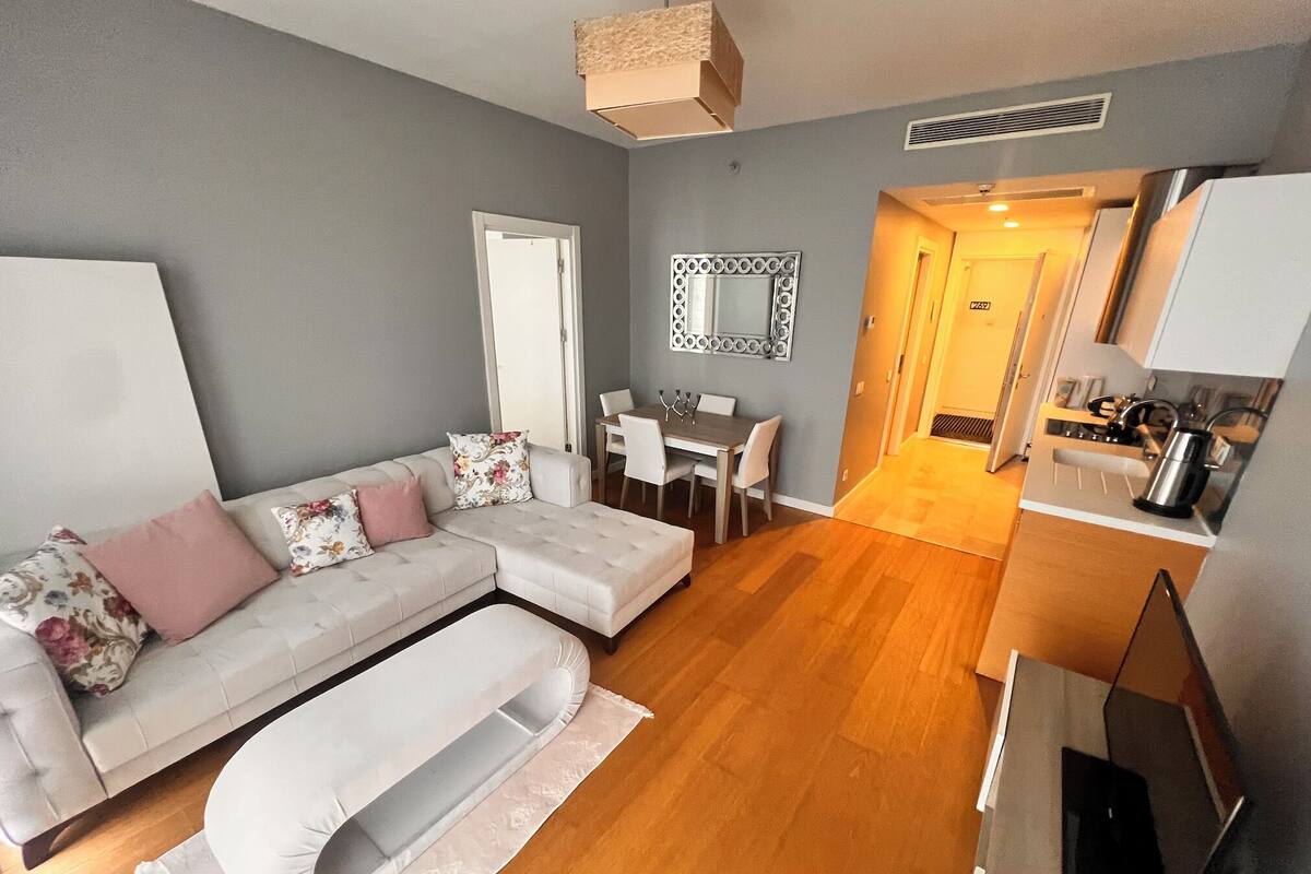 A modern living room with a sectional sofa, a dining table, and a kitchen area with a stove and microwave.