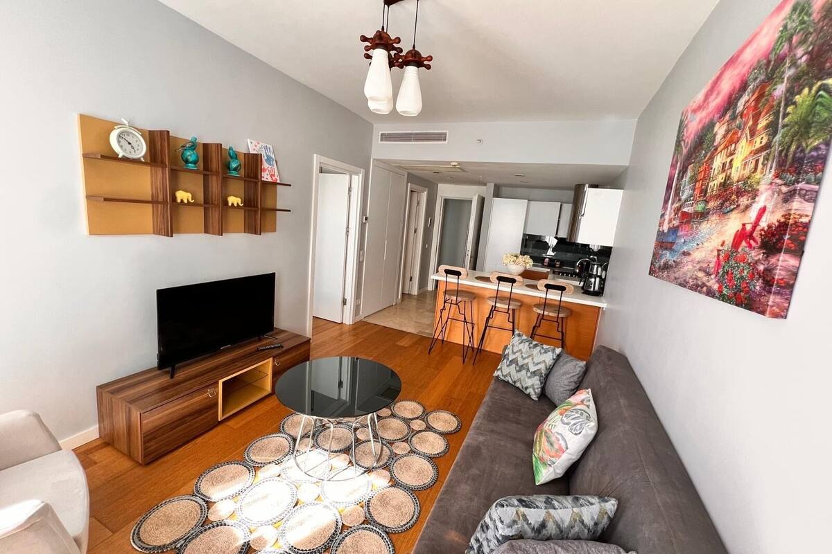 A modern living room with a flat-screen TV, wooden furniture, a round coffee table, and a patterned rug.