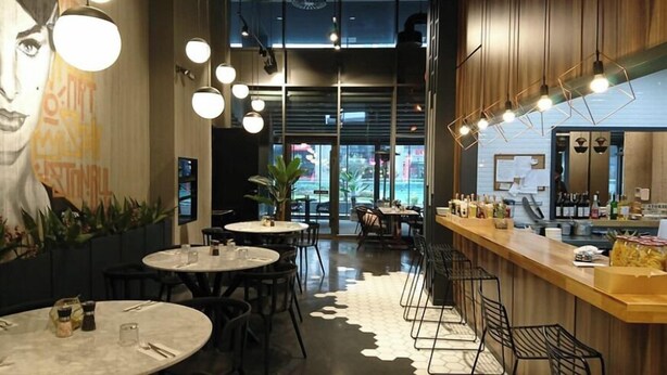 Un interior de restaurante moderno con mesas redondas, sillas negras y una zona de bar con taburetes.