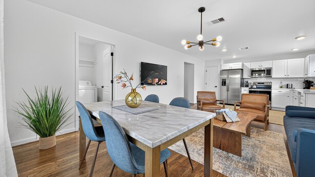 A modern kitchen with white cabinets, stainless steel appliances, and a dining area with a marble table and blue chairs. - 2BR Bright Condo 5 min to downtown HTX and NRG (Houston)