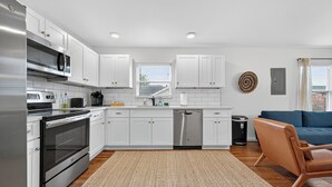 A modern kitchen with white cabinets, stainless steel appliances, and a wooden floor. - 2BR Bright Condo 5 min to downtown HTX and NRG (Houston)