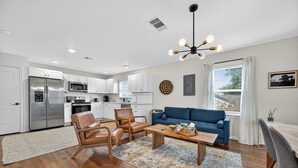 A modern kitchen with white cabinets, stainless steel appliances, and a blue sofa in the living area. - 2BR Bright Condo 5 min to downtown HTX and NRG (Houston)