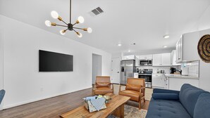 A modern living room with a wooden coffee table, leather chairs, a blue sofa, and a kitchen in the background. - 2BR Bright Condo 5 min to downtown HTX and NRG (Houston)
