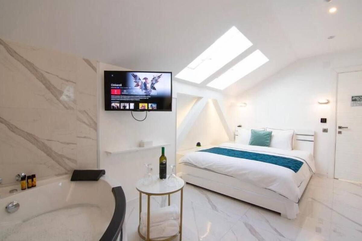 Habitación de hotel moderna con una cama grande, un televisor montado en la pared, una bañera y un tragaluz.