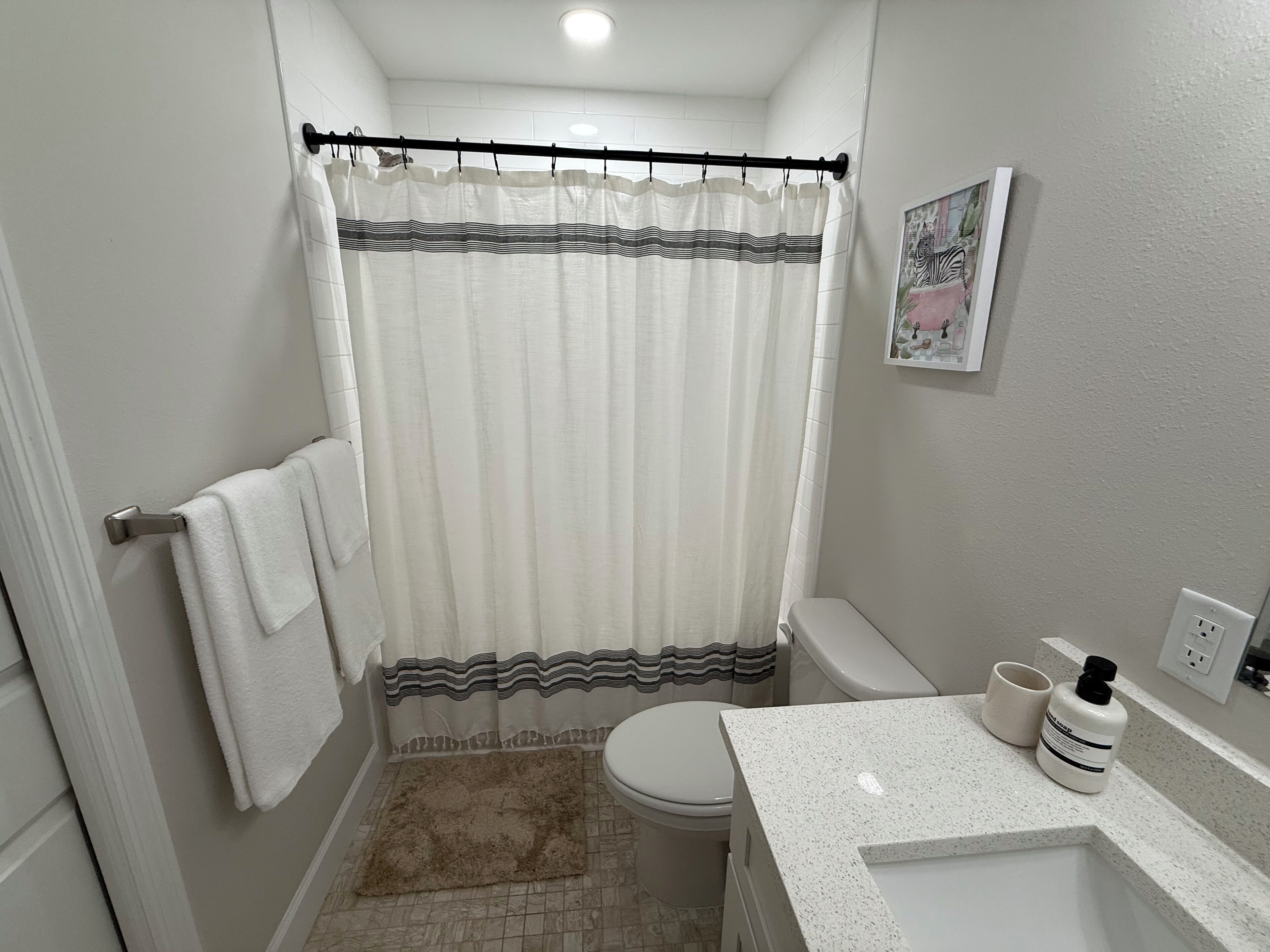 Ein kleines Badezimmer mit Duschvorhang, Toilette und Waschbecken mit Handseife.