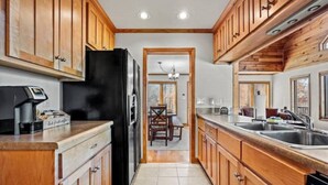 A kitchen with wooden cabinets, a black refrigerator, and a tiled floor. - Long Range Views Hot Tub Private FirePit Kid Bunks (Beech Mountain)