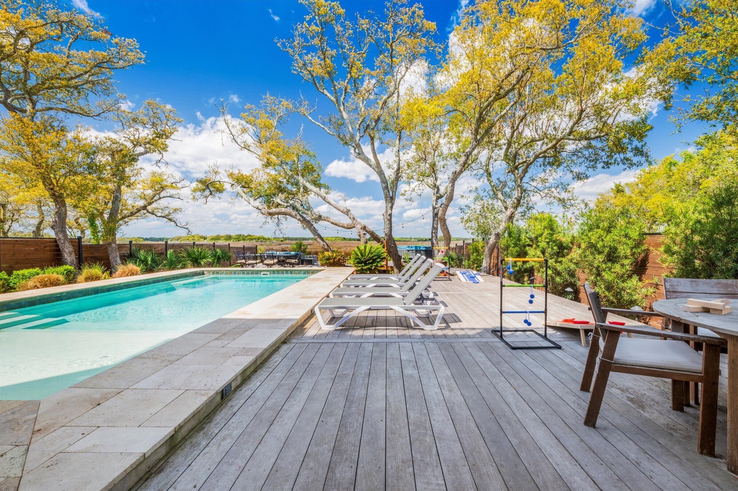 A wooden deck with a swimming pool, lounge chairs, and a table with chairs.
