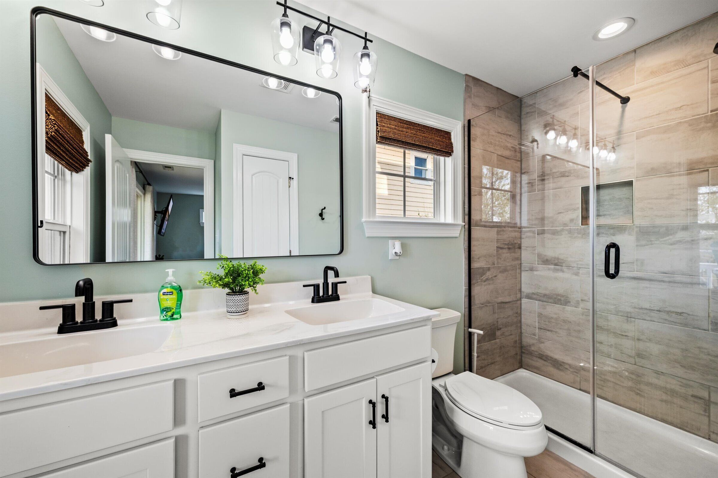 A bathroom with a white vanity, a large mirror, a toilet, and a glass-enclosed shower.