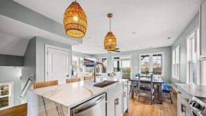 Une cuisine moderne dotée d’un îlot en marbre, d’appareils électroménagers en acier inoxydable et de luminaires suspendus en osier.