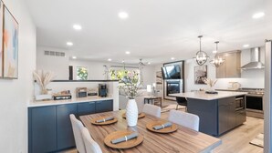 A modern kitchen with dark cabinetry, a central island, and a dining area with a wooden table and chairs. - Clear Lake Escape - Lake Views, Pool Table, Ping Pong Table, Fire Pit (Clear Lake)