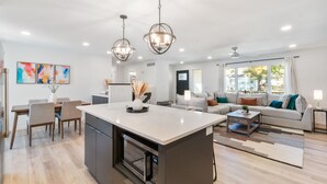 A modern kitchen with a central island, dining area with chairs, a sofa set, and a large window with curtains. - Clear Lake Escape - Lake Views, Pool Table, Ping Pong Table, Fire Pit (Clear Lake)