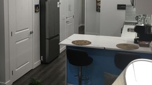 Eine moderne Küche mit weißen Schränken, einem Edelstahlkühlschrank, einer Bar mit Sitzgelegenheiten und einer Kaffeemaschine.