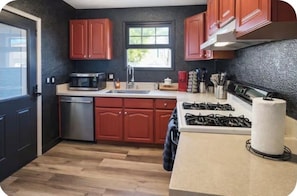 A compact kitchen with wooden cabinets, a microwave, a sink, and a gas stove.