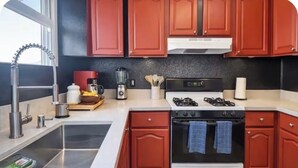 Una cocina con gabinetes rojos, un lavamanos de acero inoxidable, una estufa y una cafetera.