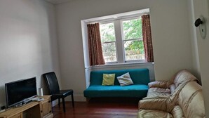 Een woonkamer met een televisie, een bank, een stoel en een raam met gordijnen.