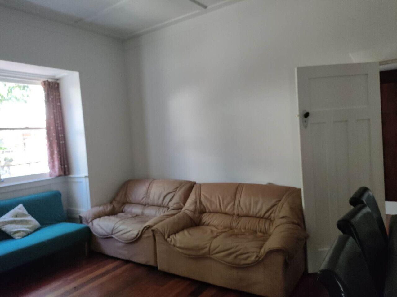 Una habitación con un sofá de cuero color beige, un sillón verde azulado y suelo de madera.