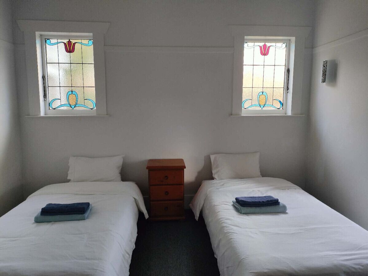 Habitación doble con dos camas, un aparador de madera y dos ventanas con vidrieras.