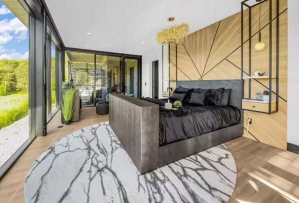 A modern bedroom with a large bed, a marble-patterned rug, and a view of the outdoors.