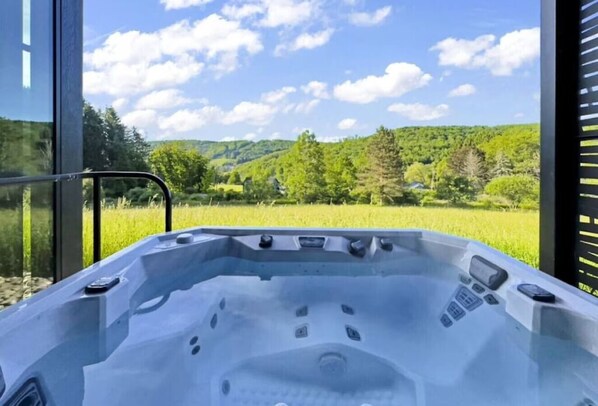Un jacuzzi con panel de control, frente a un paisaje verde y un cielo despejado.