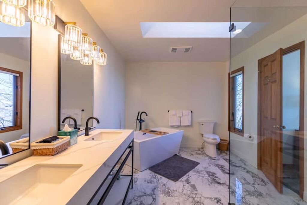 Une salle de bain moderne avec un grand miroir, deux lavabos, une baignoire et des toilettes.