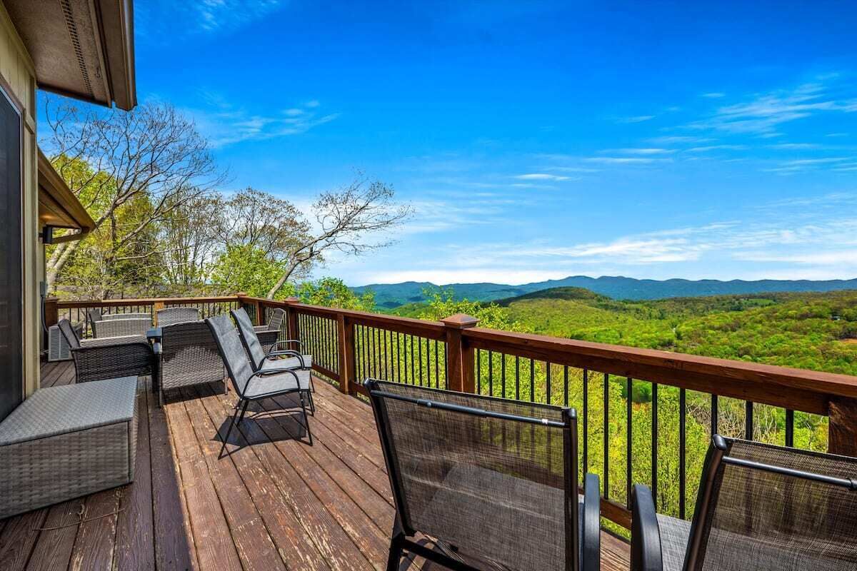 A wooden deck with outdoor furniture, a railing, and a scenic view of green hills and a clear sky.