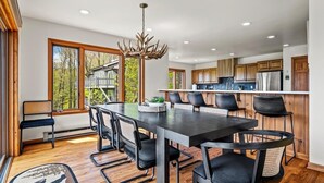 A modern kitchen with wooden cabinets, a stainless steel refrigerator, and a dining area with a large table and chairs. - Golf Club Member - Close to Ski -Mountain Views-Huge Deck (Beech Mountain)