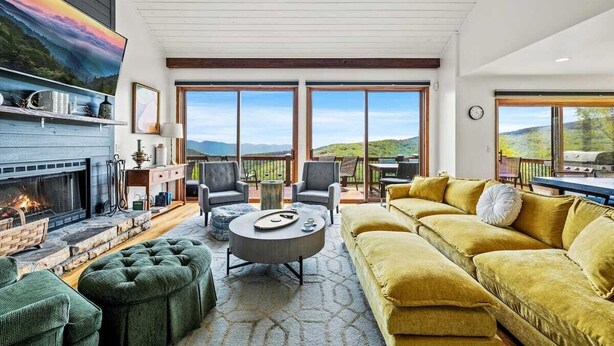 A spacious living room with a fireplace, large windows, and a yellow sofa. - Golf Club Member - Close to Ski -Mountain Views-Huge Deck (Beech Mountain)