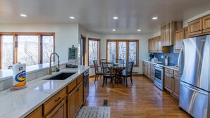 A spacious kitchen with wooden cabinets, a stainless steel refrigerator, and a dining area with a table and chairs. - Golf Club Member - Close to Ski -Mountain Views-Huge Deck (Beech Mountain)