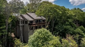 A treehouse with a wooden deck and multiple windows, surrounded by dense forest. - Golf Club Member - Close to Ski -Mountain Views-Huge Deck (Beech Mountain)