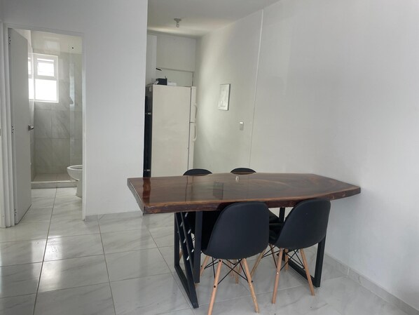 A dining area with a wooden table and black chairs, a white tiled floor, and a white wall.