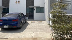 Un edificio moderno con un coche estacionado adelante, una escalera y un pequeño árbol.