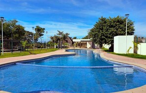 A swimming pool with a curved edge, surrounded by a paved walkway and greenery.