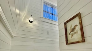 Un escalier avec des marches en bois peintes en blanc, menant à une petite fenêtre ornée de rideaux bleus.