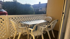 Un balcon avec une table et des chaises, une clôture blanche en treillis et une voiture rouge garée au fond.