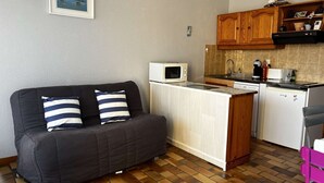 Un espace de vie compact comprenant un coin cuisine, un canapé avec des coussins à rayures et une petite table à manger.