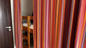 Une pièce avec un lit superposé en bois, une porte en bois sombre et un rideau à rayures.