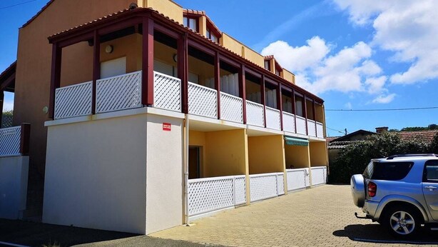 Un immeuble de deux étages avec un balcon à l’étage supérieur, un garage au rez-de-chaussée et une voiture garée devant.