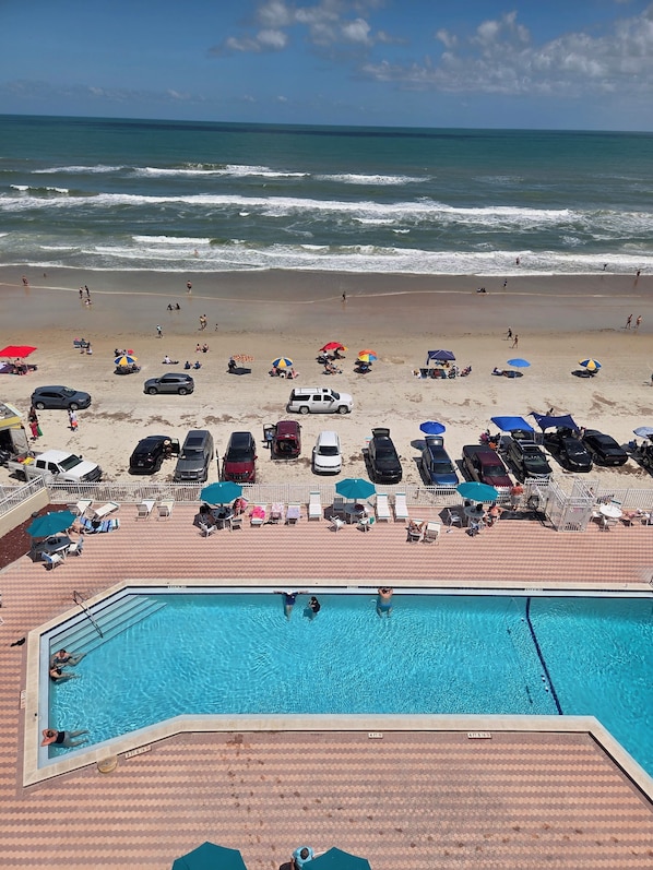 A beach with a pool, umbrellas, and lounge chairs.