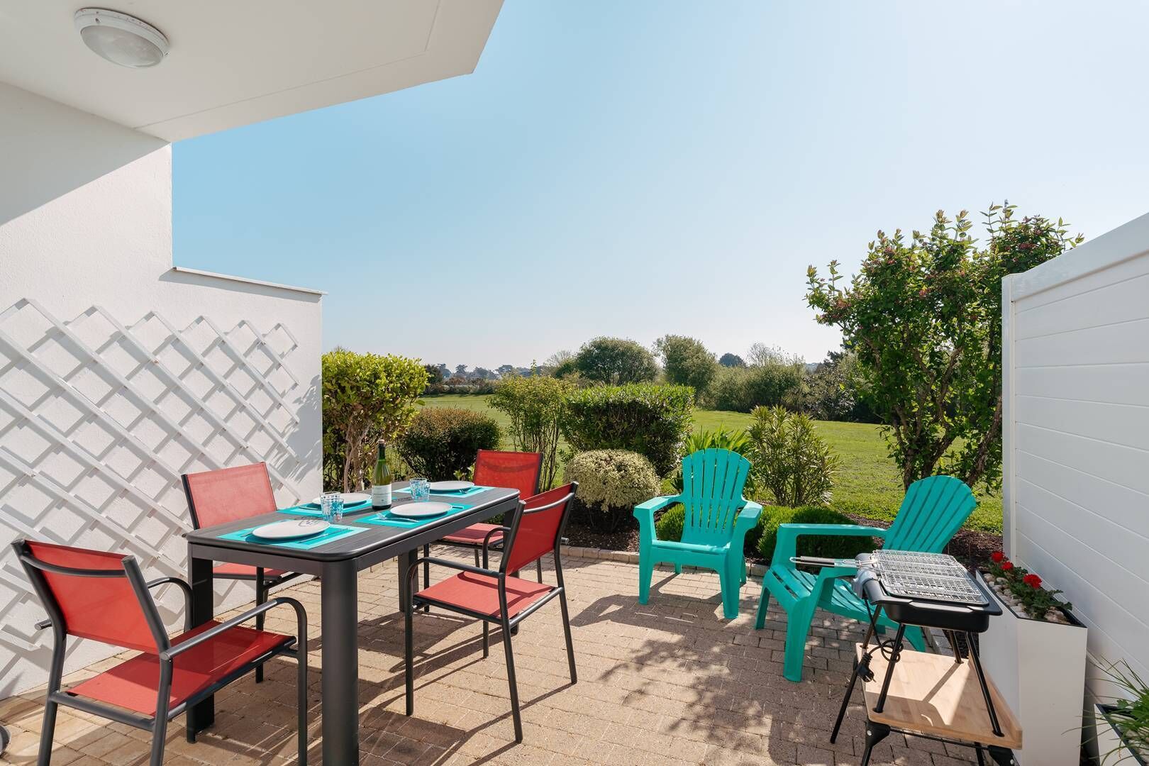 Une terrasse extérieure avec une table et des chaises, un ordinateur portable et un petit coin jardin.