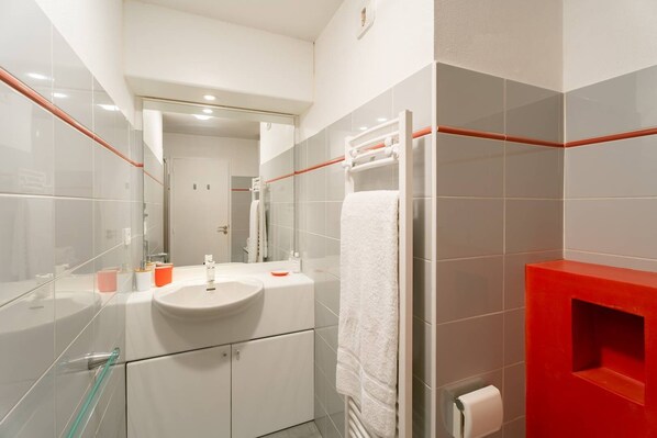 A modern bathroom with a glass shower enclosure, a white sink, and a red accent wall.