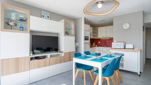 Une cuisine moderne avec un coin repas, dotée d’un téléviseur encastré, de meubles blancs et d’un luminaire au plafond au design original.